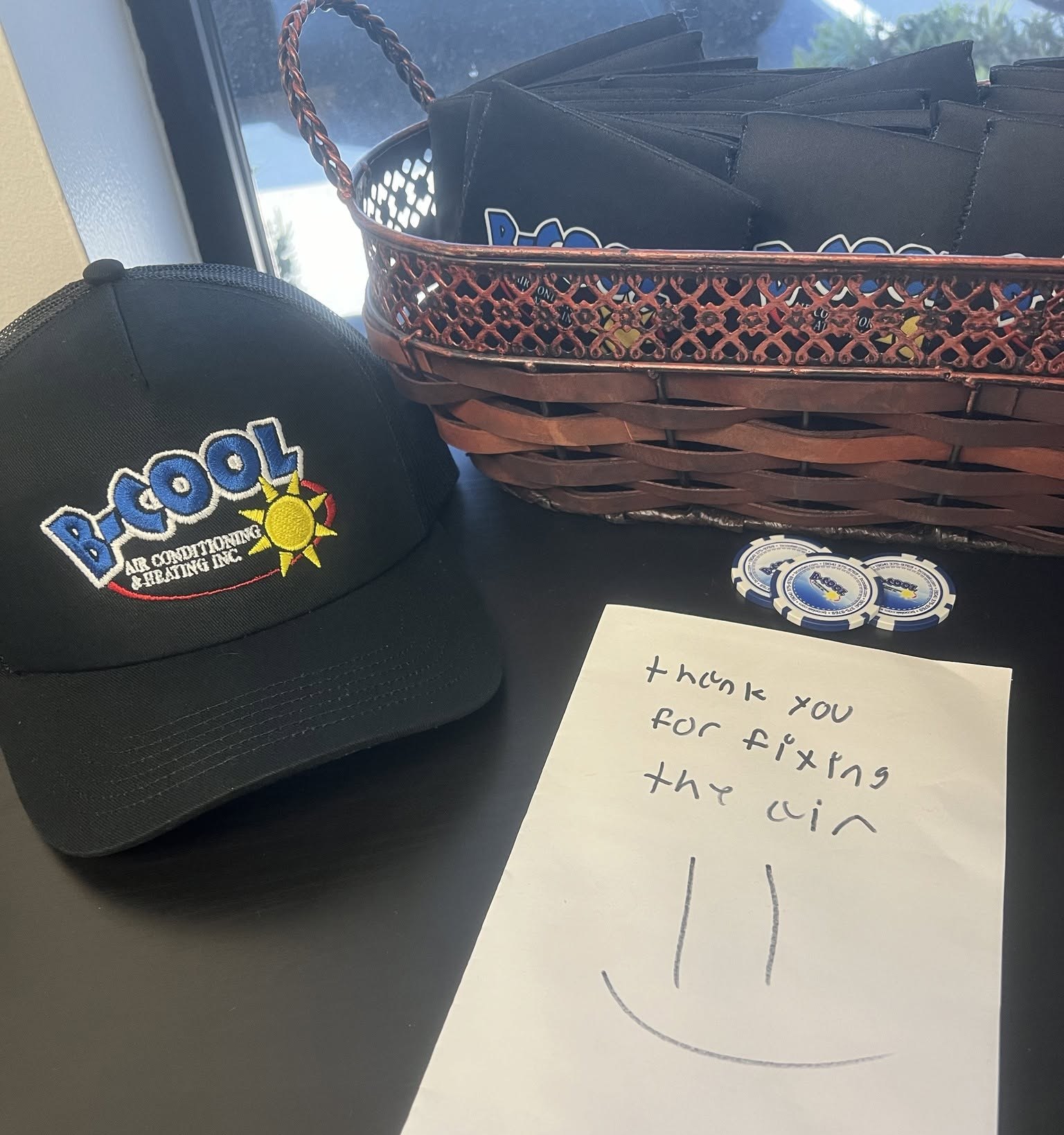 A child's handwritten thank-you note reading “thank you for fixing the air” with a smiley face, beside a B-Cool cap and a